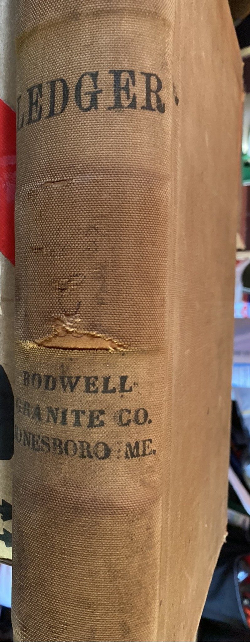 The worn tan cloth spine of a ledger, stamped in black capitals LEDGER and BODWELL GRANITE CO. JONESBORO ME., with a tear across the middle.